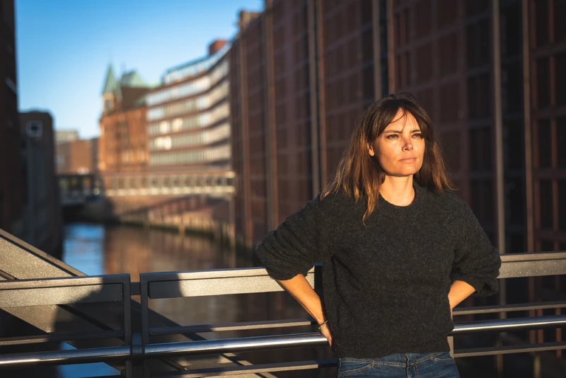Frau steht an einer Br&uuml;cke und schaut zur Sonne